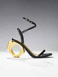Black and gold ankle strap sandals with circular sculptural heel in studio
