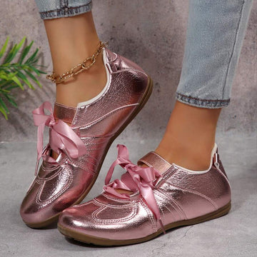 Front three-quarter view of metallic pink ribbon-lace low-top sneakers with gum soles