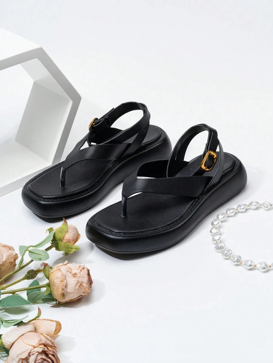 Front three-quarter view of black toe-post platform sandals with gold buckles