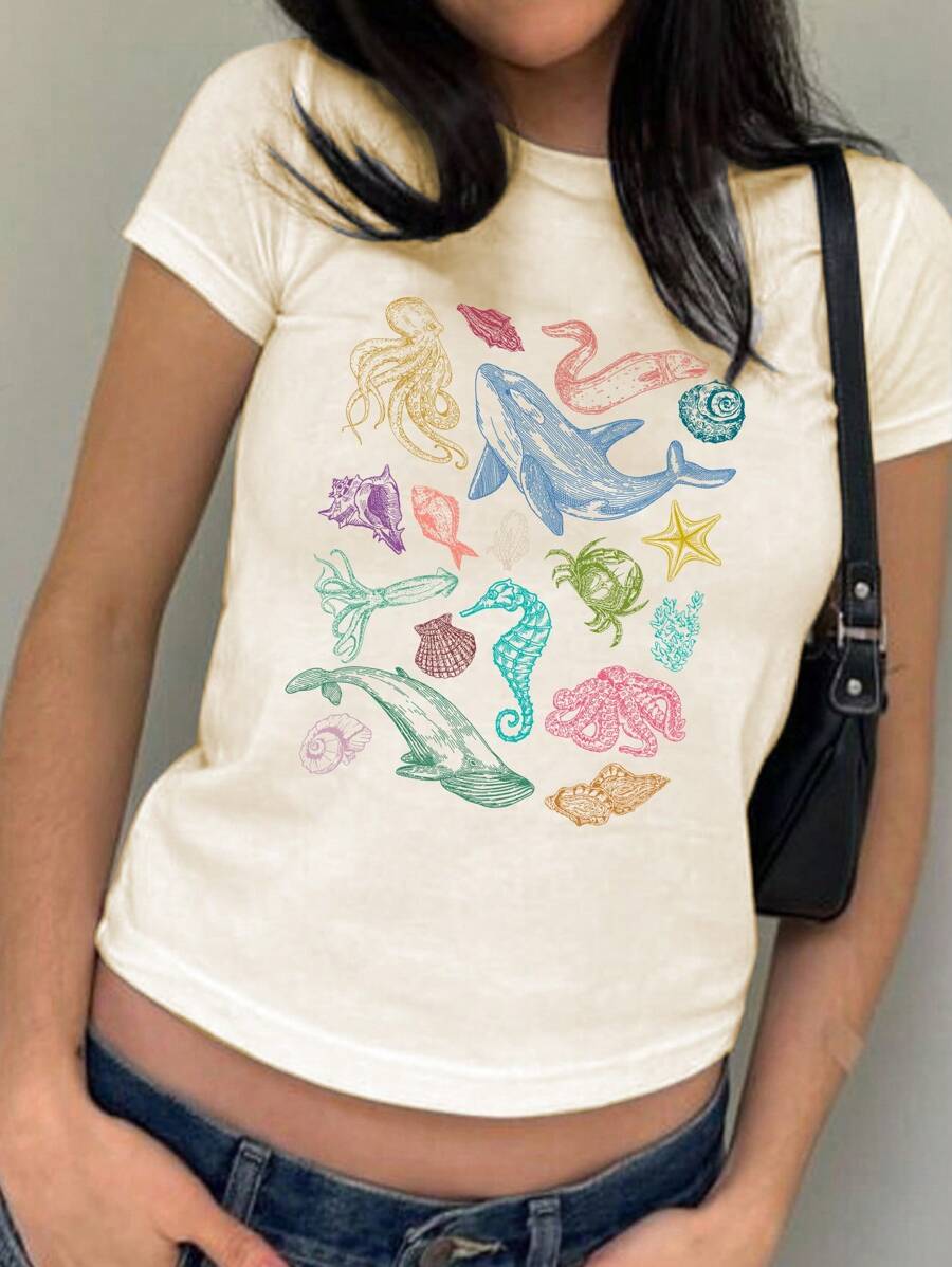 Front worn view of apricot cropped T-shirt with colorful marine-life graphic and jeans
