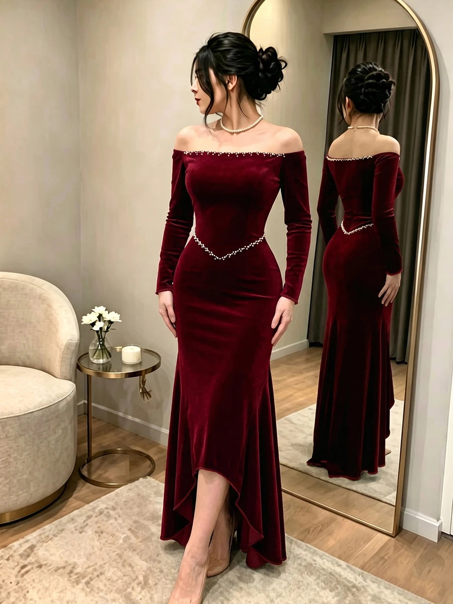 Full front view of a model in a burgundy velvet off-shoulder mermaid evening gown with pearl neckline and waist trim