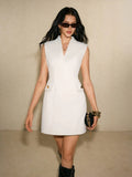 Full front view of the pale fitted mini dress with notched V neckline, gold-tone pocket buttons and black boots.