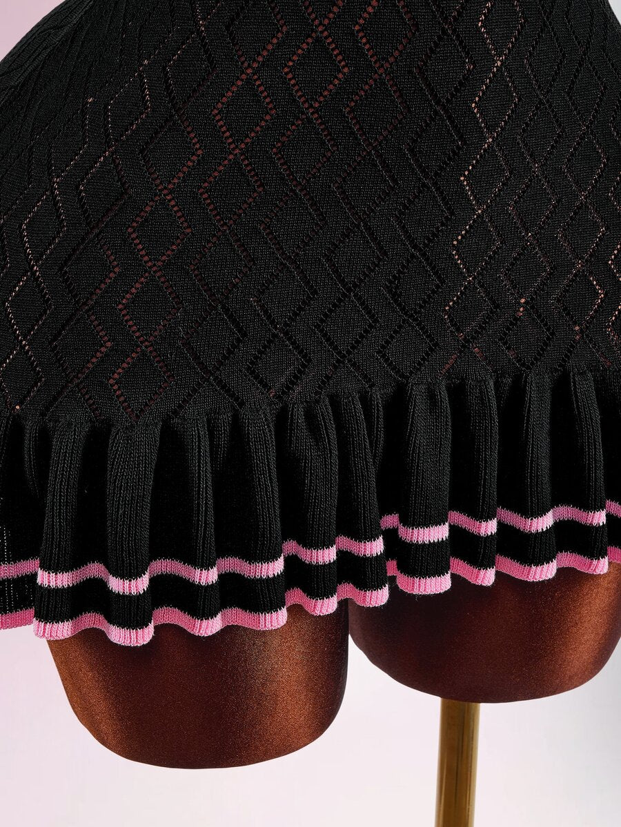 Close-up of black knit dress pleated hem with double pink stripes and pink-edged ruffle
