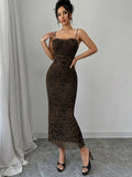 A woman models a brown and black leopard print spaghetti-strap maxi dress with a lace-trimmed sweetheart neckline, styled with black strappy heels against a gray wall and draped white fabric.