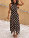 Front view of a brown and cream plaid halter dress with a fitted bodice and pointed asymmetric hem on stone steps.