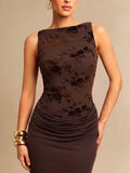 A woman wearing a sleeveless dark brown bodycon dress with a floral jacquard pattern on the bodice and gathered draping at the waist, photographed against a plain beige studio background.